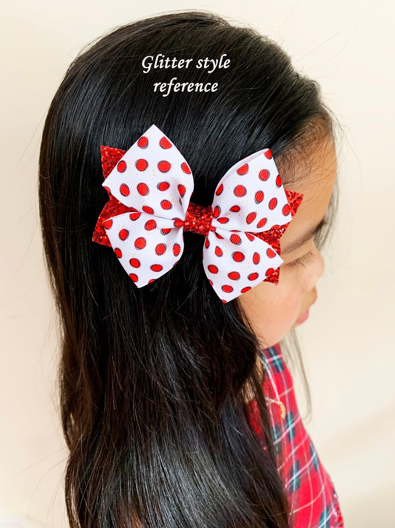 Pu&ograve; includere: Un fiocco bianco con pois rossi e dettagli glitter. Il fiocco &egrave; legato con un nastro rosso e viene indossato nei capelli di una bambina.