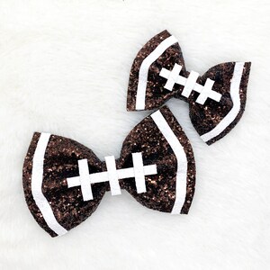 May include: Two brown glitter hair bows shaped like footballs with white stitching.