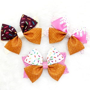May include: Three handmade hair bows in the shape of ice cream cones. The bows are made of brown, pink, and white fabric with sprinkles and a waffle cone pattern.