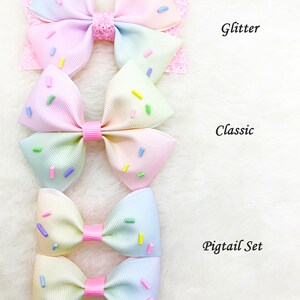 Pu&ograve; includere: Tre fiocchi per capelli arcobaleno pastello con codette. Il fiocco superiore &egrave; glitterato, il fiocco centrale &egrave; classico e i due fiocchi inferiori sono un set per codino.
