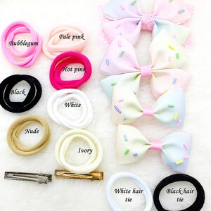 Pu&ograve; includere: Un set di accessori per capelli che include una variet&agrave; di elastici per capelli in colori come rosa bubblegum, rosa pallido, rosa acceso, nero, bianco, nude e avorio. Ci sono anche due fermagli per capelli e due elastici per capelli etichettati come "white hair tie" e "black hair tie".