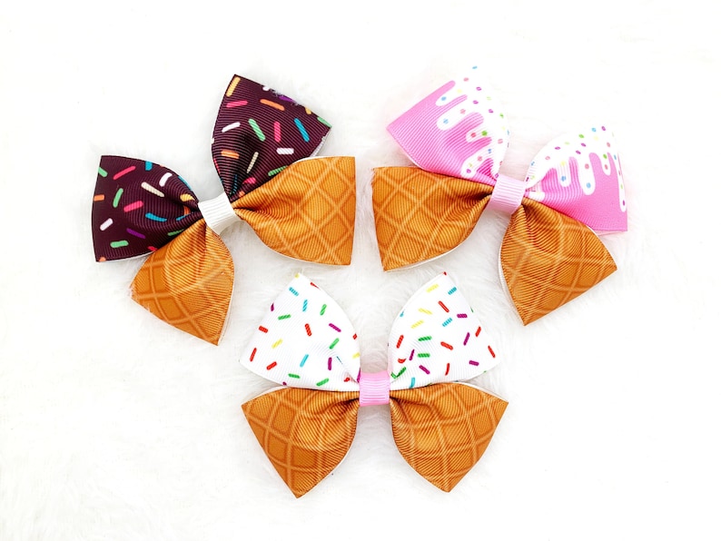 May include: Three handmade hair bows with an ice cream cone design. The bows are made of brown, pink, and white fabric with a waffle cone pattern. The bows are tied with a white ribbon.