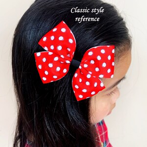 Pu&ograve; includere: Un fiocco rosso e bianco a pois con un elastico nero. Il fiocco &egrave; legato in uno stile classico e viene indossato nei capelli di una ragazza.