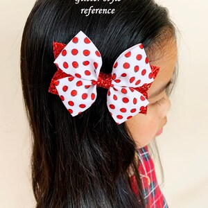 May include: A white and red polka dot bow with glitter accents. The bow is tied with a red ribbon and is worn in a girl's hair.