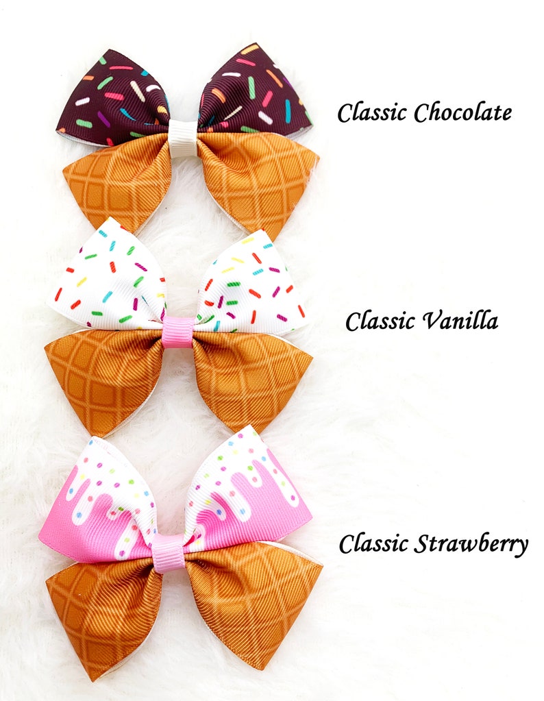 May include: Three ice cream cone hair bows with different flavors: chocolate, vanilla, and strawberry. Each bow features a waffle cone pattern and a colorful ice cream design.