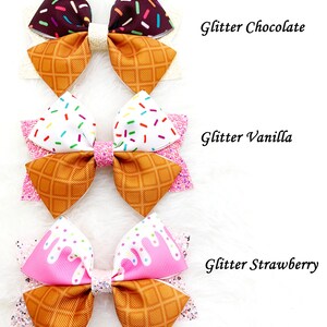 May include: Three ice cream cone hair bows with glitter. The bows are in chocolate, vanilla, and strawberry flavors. Each bow has a waffle cone pattern and sprinkles.