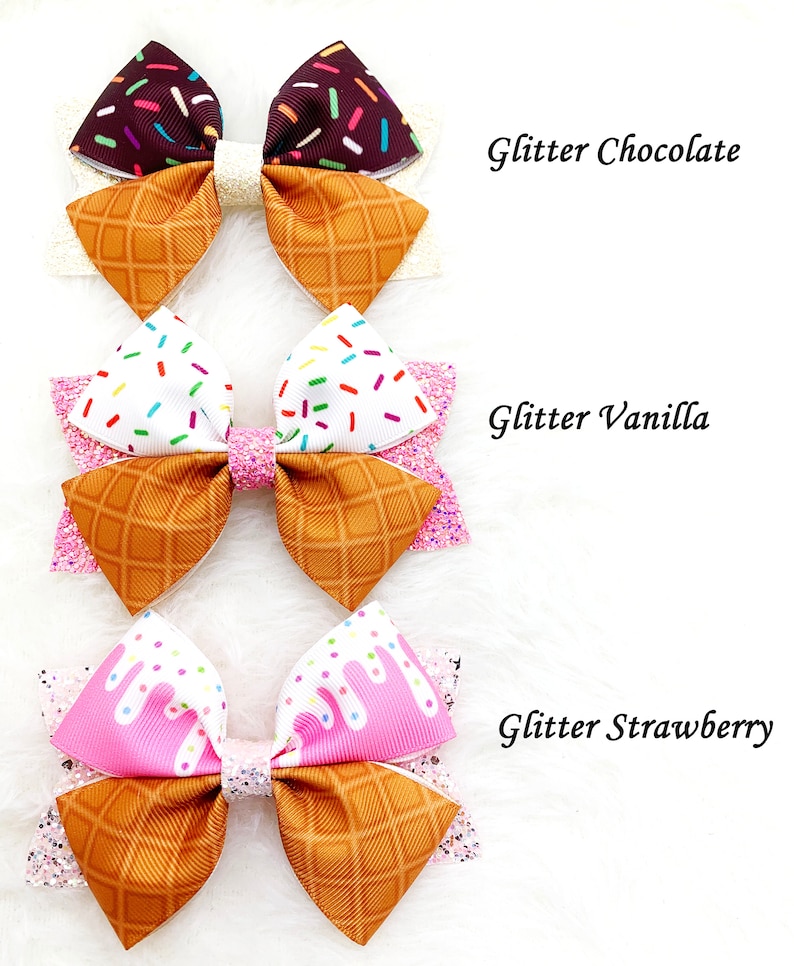 May include: Three ice cream cone hair bows with glitter. The bows are in chocolate, vanilla, and strawberry flavors. Each bow has a waffle cone pattern and sprinkles.