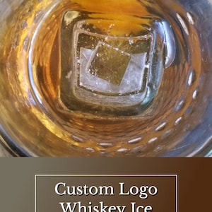 May include: A glass of whisky with an ice cube shaped like a logo. The ice cube has a square shape with a logo inside. The glass is on a brown surface. The text on the image reads "Custom Logo Whiskey Ice" and "Speakeasy Ice Molds".