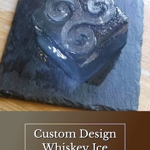 May include: A clear ice cube with a swirling design on a black slate coaster. The ice cube is a custom design whiskey ice mould. The text "SPeakeasy Ice Molds" is below the ice cube.