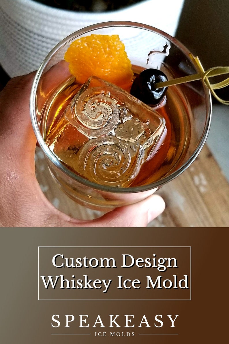 May include: A close-up of a whiskey old fashioned cocktail with a large ice cube, an orange peel garnish, and a maraschino cherry. The ice cube has a swirling design. The text "Custom Design Whiskey Ice Mold" and "Speakeasy Ice Molds" is visible below the image.