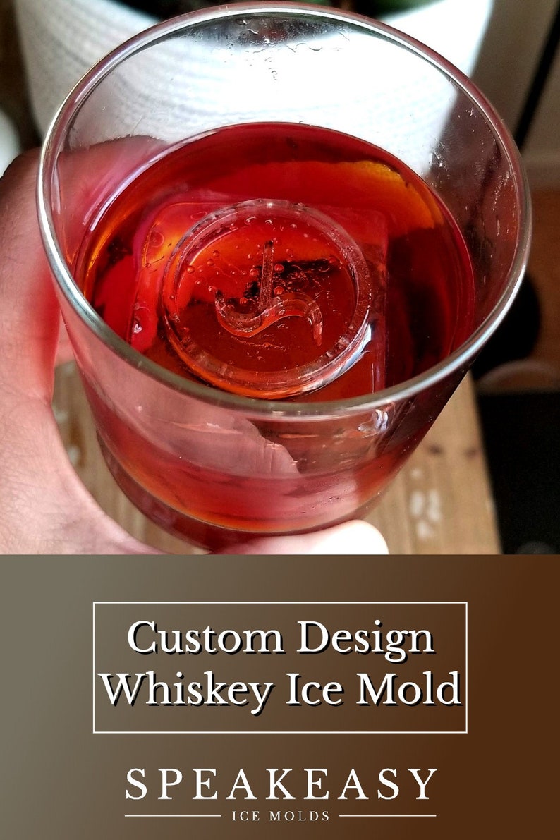 May include: A close-up of a red alcoholic drink in a glass with a custom-designed ice mould in the shape of a stylised letter "J". The ice mould is made by SPEAKEASY ICE MOLDS.