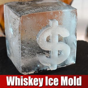 Puede incluir: Un molde de hielo transparente con un diseño de signo de dólar. El cubo de hielo está sobre una superficie negra. Molde de hielo para whisky.