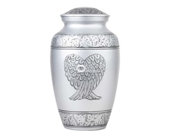 May include: Silver metal urn with an engraved design of angel wings in the shape of a heart. The urn has a decorative floral pattern around the top and bottom.