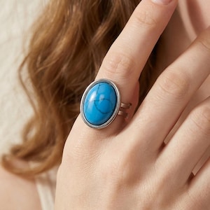Op de afbeelding: Een zilverkleurige ring met een grote, ovale, felblauwe steen met donkere, webachtige aders. De steen is gezet in een gladde, gepolijste metalen zetting en de ringband bestaat uit twee dunne, parallelle metalen draden die samenkomen.