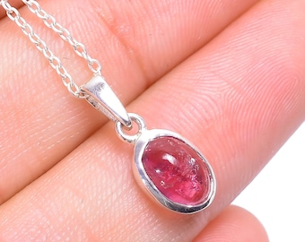 May include: A silver pendant necklace featuring a polished oval-shaped deep pink gemstone set in a smooth silver bezel. The pendant hangs from a delicate silver chain with small, uniform circular links, creating a simple and elegant jewelry piece.