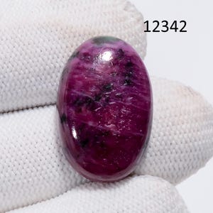 May include: Oval-shaped gemstone with a polished surface. The stone is primarily a deep magenta color, with streaks of black and hints of green. The number "12342" is printed in black in the upper right corner. The gemstone is set against a white background.