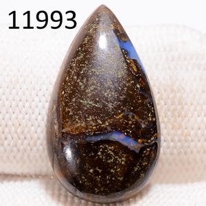 May include: A polished, teardrop-shaped gemstone. It has a dark brown base with blue, gold, and green inclusions. The number "11993" is printed in white at the top. This gemstone is likely used in jewellery. The stone is approximately 4 cm in length.