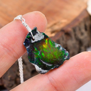 Könnte beinhalten: Eine silberne Kettenkette mit einem Anhänger aus schillerndem grün-schwarzem Opal. Der Opal ist ein raues, natürliches Stück mit einer gezackten Kante.