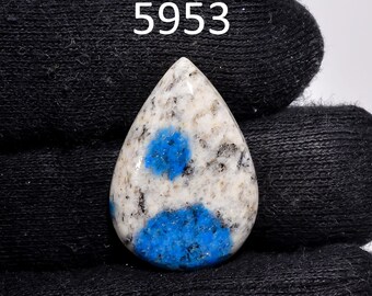 May include: A teardrop-shaped gemstone with a white base, speckled with black and featuring vibrant blue patches. The number "5953" is printed in white on the top left. The stone is held against a black fabric background.
