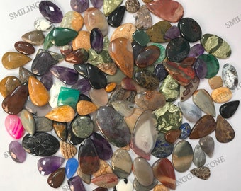 May include: A collection of colorful, natural gemstone cabochons in various shapes and sizes. The cabochons are mostly teardrop shaped and have a polished, smooth finish. The stones are a mix of colors, including brown, green, red, purple, and white.