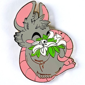 May include: An enamel pin featuring a cartoon mouse in grey and pink, holding a white flower with green leaves.