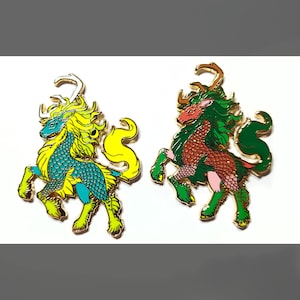 Puede incluir: Dos pines de esmalte de color dorado que representan criaturas míticas. La criatura de la izquierda es un caballito de mar verde y amarillo con una melena de pelo amarillo. La criatura de la derecha es un caballito de mar rojo y verde con una melena de pelo verde.
