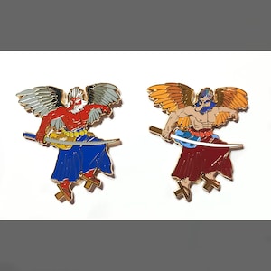 May include: Two metal pins featuring winged figures with swords. One pin has a red torso, blue skirt, and gray wings. The other pin has a brown torso, maroon skirt, and orange wings. Both pins have gold accents and are set against a white background.
