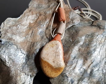 May include: A ceramic pendant necklace with a brown, white, and orange stone pendant. The necklace is made with a natural fiber cord and has two brown and orange ceramic beads.