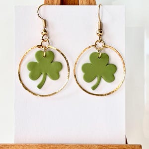 May include: Gold hoop earrings with a green shamrock charm hanging from each hoop.