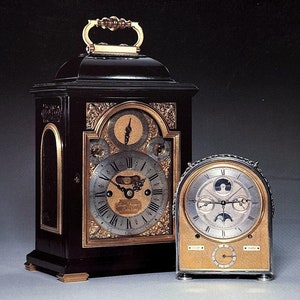 Puede incluir: Una portada de catálogo con dos relojes antiguos. El reloj más grande es de madera oscura con detalles dorados, mientras que el más pequeño es dorado. El texto dice "Important Clocks, Watches and Barometers" y "Christie's."