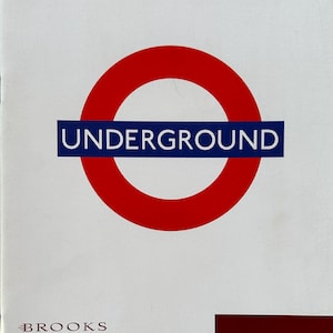 May include: A white brochure featuring the London Underground logo: a red circle with a blue rectangle reading "UNDERGROUND." Text includes "BROOKS," details of a sale of London Underground signs and ephemera at the Natural History Museum on December 5th, 1995.