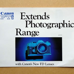 Op de afbeelding: Een witte advertentie met het Canon FTb-logo en de tekst "Verlengt het fotografische bereik". De afbeelding toont een vintage camera met een lens, tegen een blauwe achtergrond. De tekst "met Canon's New FD Lenzen" staat onderaan.