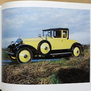 Könnte beinhalten: Ein offenes Buch mit einem Foto eines gelben Rolls-Royce Phantom I Two-Seater Coupe Cabriolet. Das Auto hat schwarze Akzente und steht auf einer Wiese. Text auf der linken Seite beschreibt das Auto.