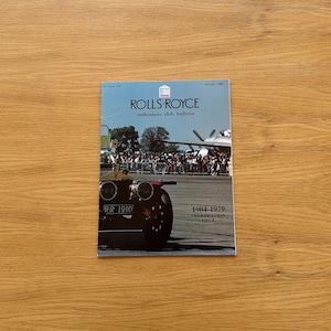 Puede incluir: Una portada de revista con un coche Rolls-Royce antiguo y el texto "ROLLS-ROYCE enthusiasts club bulletin". La portada incluye el texto "1904-1979 CELEBRATION ISSUE" y "RR 1910". El fondo muestra una multitud y un avión.