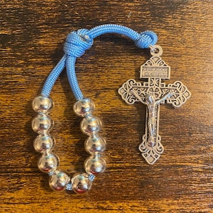 May include: A light blue beaded bracelet with a silver cross charm. The cross has the inscription "JESUS NAZARENUS REX JUDAEORUM".