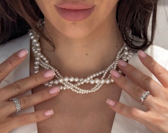 May include: A multi-strand pearl necklace with a delicate, layered design. The necklace is made of white pearls and is worn by a person with a white shirt.
