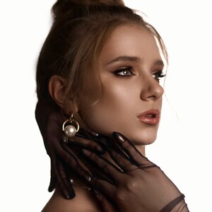 May include: A woman with a bun in her hair wears a pair of black sheer gloves. She is wearing a gold earring with a pearl.