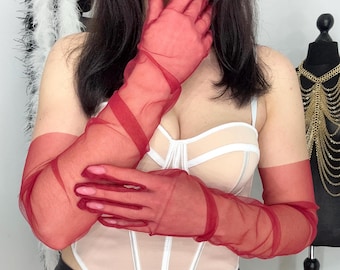 May include: Sheer red opera gloves with a long, elegant design. The gloves are made of a lightweight, see-through fabric and feature a wrap-around detail. The gloves are a vibrant red color and are perfect for a special occasion.