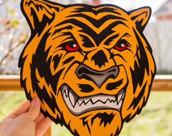 May include: A close-up of a yellow and black tiger face patch with red eyes. The tiger is snarling with its teeth showing.
