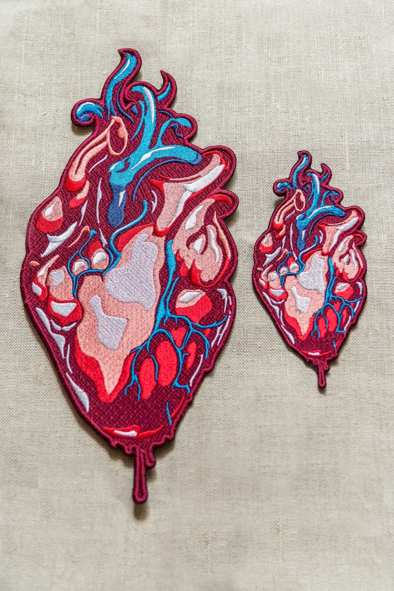 Op de afbeelding: Twee geborduurde patches van anatomische harten, een groter dan de andere. Beide zijn rood, roze en blauw met druppelende randen.