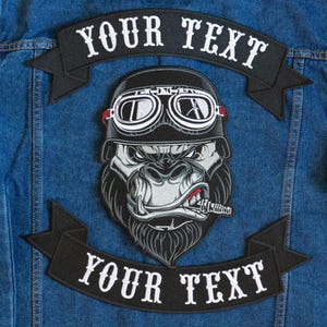 May include: Embroidered patch featuring a gorilla wearing a motorcycle helmet and goggles, smoking a cigar. The patch has the text "YOUR TEXT" on a banner above and below the gorilla image. The patch is on a blue denim jacket.