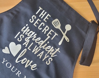 May include: Black kitchen apron with white embroidery that reads "The Secret Ingredient Is Always Love" and a space for "Your Name".