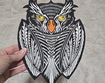May include: Black and white embroidered owl patch with an orange beak and yellow eyes. The owl is surrounded by a white and black patterned design.