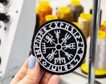 May include: A circular black embroidered patch featuring a white Vegvisir symbol at the centre, surrounded by a border of white runic characters. The design is stitched with high-contrast white thread against a solid black fabric background.