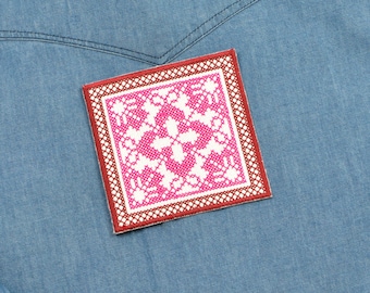 May include: A pink and white embroidered patch with a red border. The patch is stitched onto a blue denim fabric.