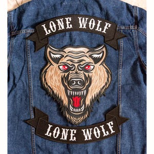 May include: A denim jacket with a large embroidered patch featuring a wolf's head with red eyes and the text "LONE WOLF" above and below the wolf. The patch is in shades of brown, tan, and black.