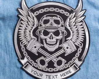 May include: A black and silver embroidered patch with a skull wearing a helmet and goggles, wings, and crossed pistons. The patch is encircled by a chain design and has the text "YOUR TEXT HERE" on a banner.