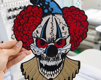 May include: An embroidered patch featuring a sinister clown face with bright red curly hair, a blue and black polka-dot hat, piercing red eyes, a black nose, and a wide, toothy grin. The clown wears a tan ruffled collar against a black background.