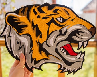 May include: A close-up of an embroidered tiger head patch. The patch is yellow, black, white, and red. The tiger's mouth is open, showing sharp teeth and a red tongue.