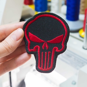 May include: A black and red embroidered skull patch with a red outline. The skull has a red nose and eyes.